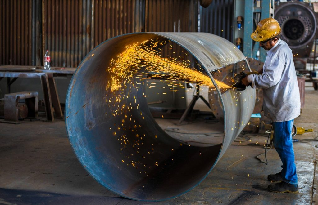 Worker grinding metal pipe